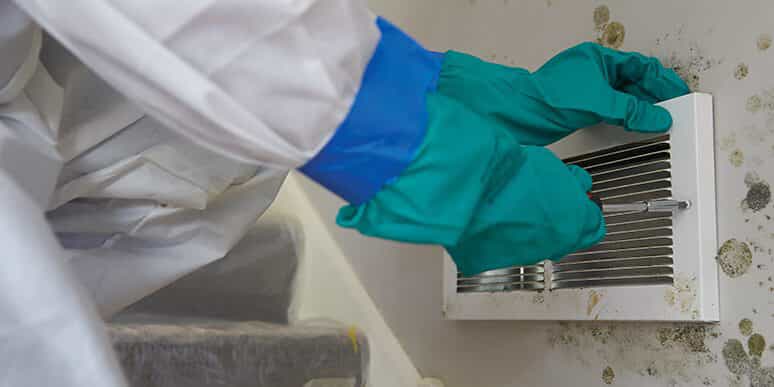 A person with gloves cleaning off a moldy vent